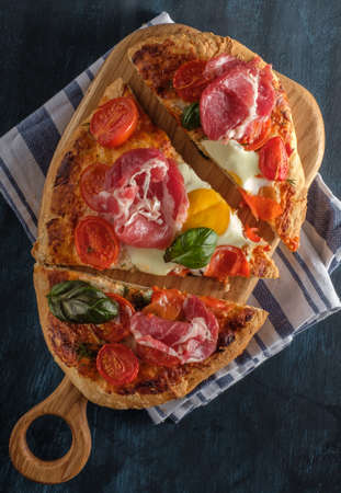Sliced Homemade tasty pizza with bacon, egg, cheese, tomatoes and basil  on dark background. Top view.の写真素材