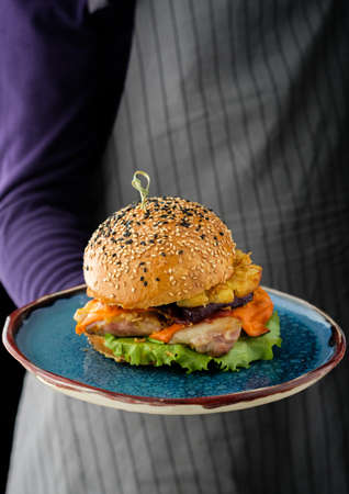 Chicken burger with pineapple. Men's hands hold a tray with a cheeseburger.の写真素材