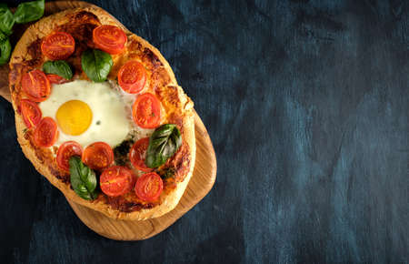 Homemade tasty pizza with egg, cheese, tomatoes and basil on dark background. Top view.の写真素材