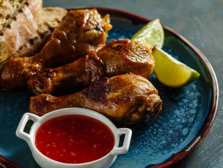 Fried spicy chicken legs in a ceramic dish with red sauce and lime.の写真素材