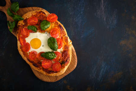Homemade tasty pizza with egg, cheese, tomatoes and basil on dark background. Top view.の写真素材