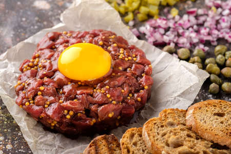 Fresh Beef Tartar is served with yolk, fried bread, pickled cucumbers and capers.の写真素材
