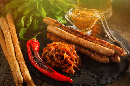 Grilled sausages and stewed cabbage with a mug of beer on a wooden table. Rustic style. Snacks for the Oktoberfest.の写真素材
