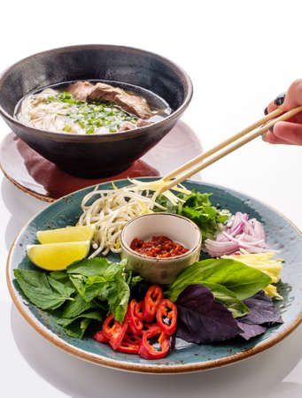 Traditional Japanese soup ramen with noodles and beef. Preparation of soup Ramen. A woman's hand puts herbs in a bowl of soup.の写真素材