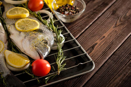 Fresh Raw Dorado with lemon, thyme, cherry and rosemary on the wooden table. Copyspace.の写真素材