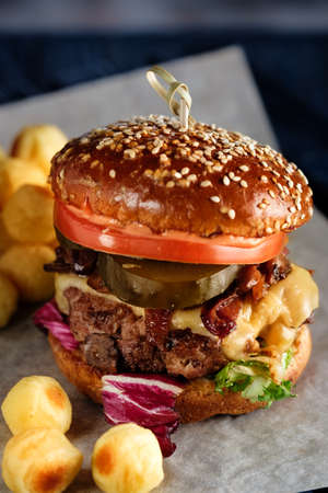 Homemade delicious juicy burger with beef, cheese, tomato and caramelized onion and potato ballsの写真素材