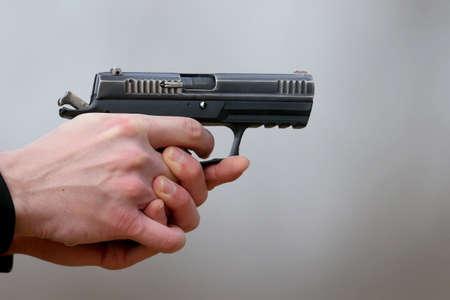 Close-up Photo of a pistol shooting with two hands, the shells emanating from the shutter and blue smoke on a blurred background.の写真素材