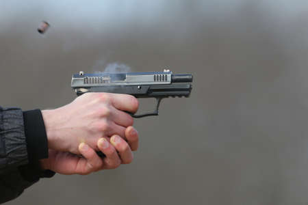 Close-up Photo of a pistol shooting with two hands, the shells emanating from the shutter and blue...