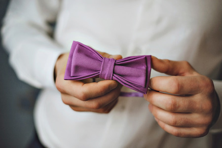 butterfly of violet color on a neck at the man. Man wears purple, purple bow-tie. The bridegroom going to the wedding. Wedding morning. The man straightens his tie.の写真素材