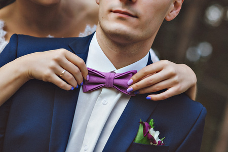 Pretty bride adjusting the bow tie. Serenity, lilac, blue in the image. A pair of lovers in a pine forest.  The bride was behind me. Blue suit, white dress and serenity accessoriesの写真素材