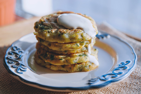 Vegetarian vegan diet snack, fritters on a plate of zucchini with herbs. Snack on a wooden surface, with sour cream.の写真素材