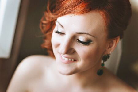 portrait of red-haired young woman bride, smiling, looking down.
