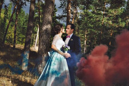 Young man and woman walking in a pine forest, wedding story. Colored smoke. Kissの写真素材