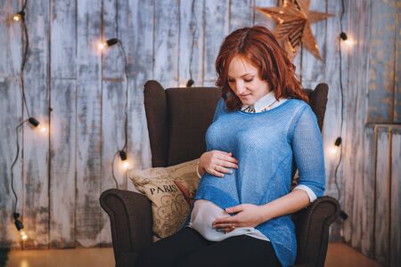 Young woman pregnant in blue outfit. Red hair. Smiling happily.の写真素材