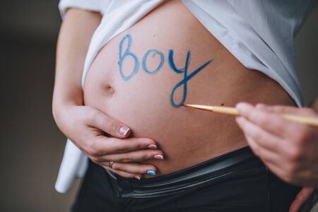 The husband is drawing on the belly of his pregnant wife, the word boy. Blue paint color