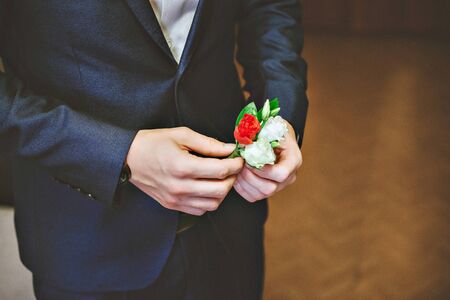 men's blue suit, red tie, white shirt. The groom adjusts his boutonniere of rosesの写真素材