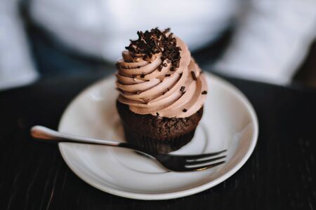 Chocolate cupcake on a saucer with a dessert fork. On a dark background.