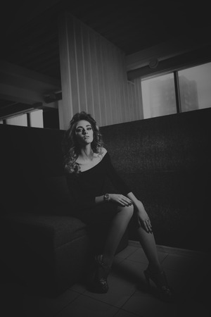 Young beautiful woman in dress sitting on the couch. Black and white photographyの写真素材