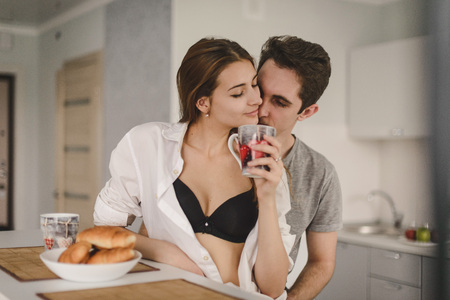 Loving couple in the kitchen. Young man and woman eating a croissant and fresh pastries. Drink tea, coffee. Love. Happinessの写真素材