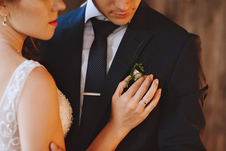 Hands of the bride and groom. The bride adjusts the boutonniere on the jacket of the groomの写真素材
