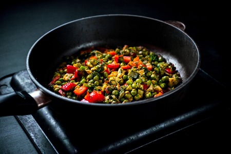 Vegetable stew with green peas, red pepper, onion and zucchini, and spices. In a frying pan on a black backgroundの写真素材