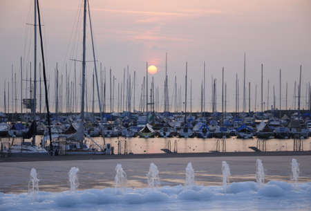 Sunset with foreground of yachts and pavement fountain at Ouchy Port at Lausanne, Switzerlandの写真素材