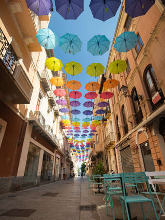Iglesias, Italy: Colorful umbrellas hanging over a street in old Iglesias city in a sunny dayの写真素材