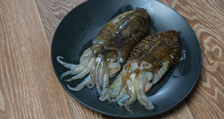 Fresh cuttlefish on a black plate on a wooden table.