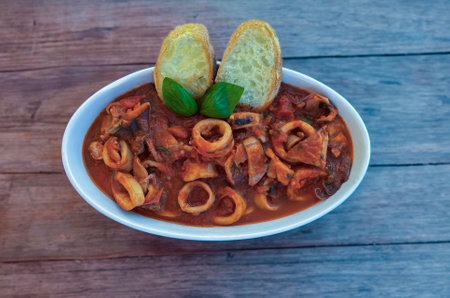 Spicy squid soup with tomato and basil on white plate and dark backgroundの写真素材