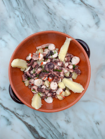 Octopus appetizer with potatoes and capers in terracotta dishの写真素材