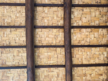 Close-up of a traditional bamboo roof supported by dark wooden beams, showing craftsmanship and natural materialsの写真素材