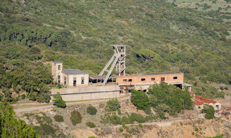 Rusty headframe of an abandoned mine shaft in Montevecchio, Sardinia, Italy, surrounded by lush vegetationの写真素材