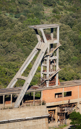 Rusty headframe of an abandoned mine shaft in Montevecchio, Sardinia, Italy, surrounded by lush...