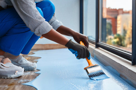 Worker applying blue epoxy resin on a wooden floor using a brush in a modern apartmentの写真素材