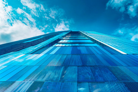 Modern glass building against bright blue sky with white clouds