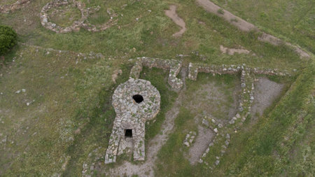 Aerial view of a Nuragic sacred well structure in Sardinia, Italy, surrounded by green grass and ancient stone ruins.の写真素材