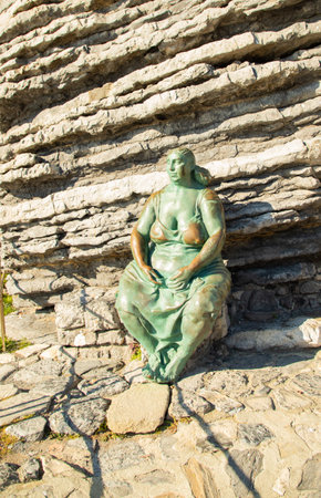 Bronze statue of Mater Naturae, symbol of nature and femininity, set against rocky cliffs in Portovenere.の写真素材