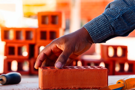Gloved hand positioning perforated red brick during masonry work at construction siteの写真素材