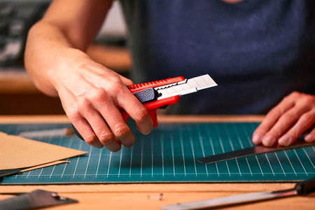 Close-up of woman's hand using cutter knife on wooden surface during crafting