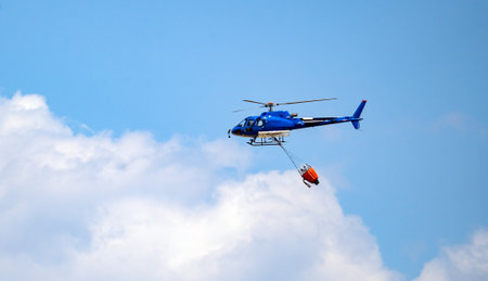 Firefighting helicopter flies with water bucket above wind turbines and forested hillsの写真素材