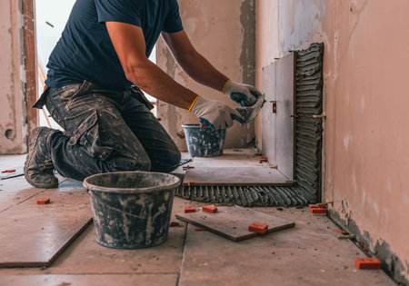 Construction worker laying ceramic tiles on a wall using adhesive and spacers during renovation