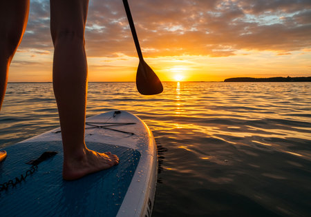 Silhouette of paddleboarder on tranquil water during vibrant sunset, feet on the SUP board