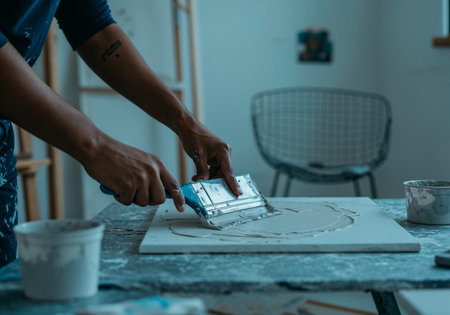 Close-up of hands applying plaster or texture paste on canvas for abstract wall artの写真素材