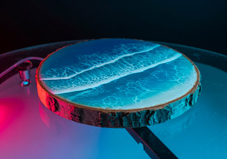 Close-up of artist pouring vibrant blue and green resin onto a wooden round boardの写真素材