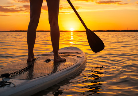 Silhouette of paddleboarder on tranquil water during vibrant sunset, feet on the SUP board