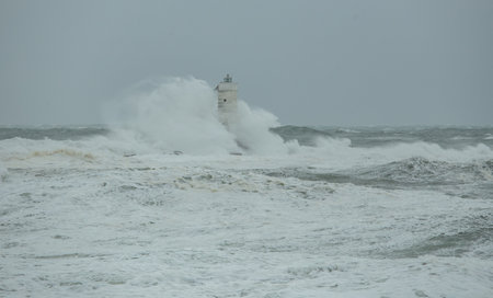 Towering waves smashing into lighthouse under heavy storm and gray skies