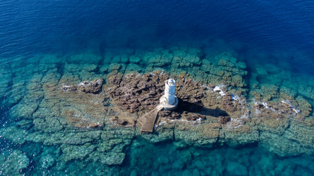 Aerial view of the historic Mangiabarche Lighthouse surrounded by turquoise sea and rocky coastの写真素材