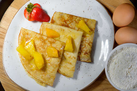 Pancakes on Shrove Tuesday with the ingredients on a plate on a wooden Board with eggs and flour