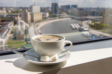Cup of coffee on the windowsill in a tall building overlooking the city from the riverの写真素材