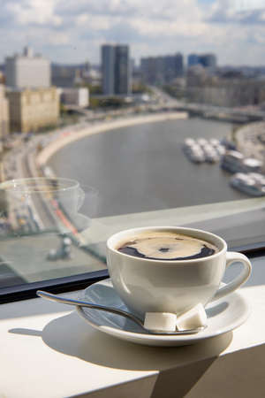 Cup of coffee on the windowsill in a tall building overlooking the city from the riverの写真素材